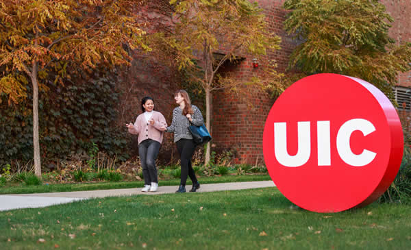 Two students walking together on campus near UIC logo